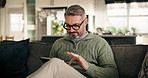 Relax, scroll and tablet with man on sofa in living room of home for entertainment or streaming. App, social media review of movie and weekend with mature person in apartment to manage subscription