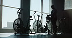 Ready, stationary bike and silhouette of woman in gym for exercise equipment, cardio and fitness. Begin, cycling machine and performance with person walking for wellness club and start training