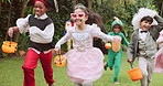 Girl, friends and running at halloween, play and excited for trick or treat event for sweets in garden. Kids, group and lantern basket on lawn for costume party, candy and happy with race for fun