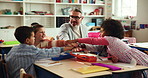 Happy man, teacher and children with hands together in classroom for team motivation at school. Male person, educator or group of learners with pile, stack or applause for education or learning