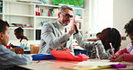 Education, high five and laughing students with teacher in classroom for development or learning. Celebration, funny or success with children and professor at desk in class of school for study
