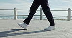 Person, legs and walking with shoes on beach promenade for travel, fresh air or outdoor stroll. Feet, sneakers and movement with fashion or style on ocean coast for commute, trip or seaside journey