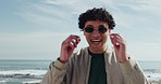 Portrait, sunglasses and man at beach with smile, ocean and fresh air in holiday. Happy, laughter and person at seafront with mockup, confident and positive energy for the spring break vacation.