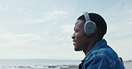 Thinking, black man and headphones at beach for travel ideas, holiday vision and listening to music. Thoughts, male person and walking for fresh air, streaming podcast and reflection of vacation trip