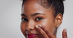 Beauty, girl and apply face cream in studio for hydration treatment, moisturizer or hyaluronic acid. Skincare, black woman and lotion on white background for healthy skin, self care routine and glow