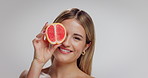 Woman, face and skincare with grapefruit in studio, smile and mockup space with nutrition on white background. Girl, model and happy with organic fruit for vitamin c benefits, beauty and wink in USA