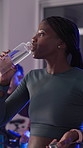Active, woman and drinking water at spin class in gym for hydration, intense workout or break. Night fitness, sweating and athlete with liquid for thirst, cycling recovery or training rest with bokeh