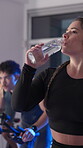 Bike, woman and drinking water at spin class in gym for hydration, intense exercise and break. Night fitness, sweating and athlete with liquid bottle for thirst, cycling recovery and cardio challenge
