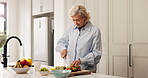 Chopping, food and fruit salad with woman in kitchen of home for diet, health or nutrition. Breakfast, cooking and cutting with mature person at counter in apartment for natural or organic meal prep