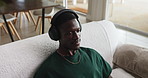 Relax, music and black man with headphones in home, streaming service or sound above in house. African person, audio and listening to radio on sofa for chill, playlist and hip hop song in living room