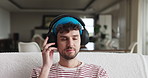 Headphones, relax and man on sofa in home with listening to music, playlist or radio on weekend. Happy, audio tech and male person streaming album, podcast or song online in living room at apartment.