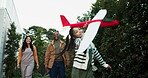 Happy, family and child with airplane, park and play with parents on vacation, together and bonding. Running, girl or fun with toy in nature, woman and man with smile on holiday, game and outdoor