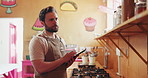 Man, chef and tablet with research for online recipe, cooking class or checklist in cafeteria. Male person, culinary artist and checking jars of spices on shelf with technology for food ingredients