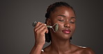 Black woman, massage and skincare with jade roller in studio for anti aging on a gray background. Female person, African model or space with beauty tool for facial treatment or lymphatic drainage