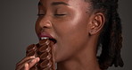 Beauty, black woman and eating chocolate bar for nutrition, healthy diet or antioxidants. Cosmetics, candy and model in studio with sweet food, cacao dessert or snack for skincare on dark background