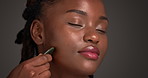 Black woman, massage or beauty with gua sha in studio for anti aging on a gray background. Female person, African model or relax with smile or skincare tool for facial treatment or lymphatic drainage
