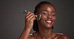 Happy, black woman or skincare with jade roller in studio for anti aging on a gray background. Female person, African model or space with smile for beauty tool, facial treatment or lymphatic drainage