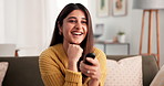 Laughing, remote and watching tv with woman on sofa in living room of home for streaming. Comedy, entertainment and humor with happy Indian person in apartment for video subscription service