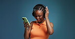 Black woman, dancing and happy in studio with headphones, phone and music on playlist. Smile, African girl and positive on blue background with technology, mobile and online streaming for tunes. 