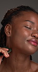 Black woman, gua sha and facial massage with makeup in studio for treatment on a gray background. Female person, African model or smile with jade stone for anti aging, skincare or lymphatic drainage