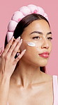 Woman, cream and skincare with headband in studio, thinking and application on pink background. Person, beauty and lotion with cosmetics, moisturizer and reflection with product for dermatology