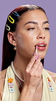 Beauty, face and woman in studio with lip gloss, hydration and plumping with cosmetic product. Smile, gen z and girl on purple background with mouth treatment, color and shine finish in makeup.