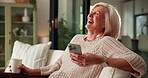 Phone, funny and coffee with old woman on sofa for relax, social media meme and morning drink. Happiness, online comedy video and drinking tea with senior person in living room of home for laugh