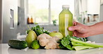 Green, ingredients and hand with juice on kitchen counter, detox or healthy drink for wellness benefits. Nutrition, gut health or person in home with bottle for liquid, fruits and vegetables for diet