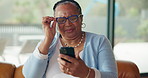 Senior woman, glasses and phone for reading, scam message or fake news on sofa in living room. Annoyed, notification and elderly african person with technology, online fraud and doubt in home