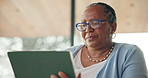 Senior black woman, tablet and search in home with glasses, notification or scroll with low angle. African person, tech and typing in living room with application, ebook or contact at apartment