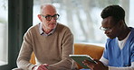 Talking, tablet and caregiver with mature man in home for consulting, medical check up and help. Retirement, sofa and nurse with person on tech for wellness, online diagnosis and healthcare support