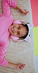 Face, headphones and child above in bed at home for streaming service, online sound and radio. Top view, happy girl and kid listening to audio, song and dance to music playlist in bedroom to relax