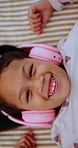 Face, headphones and child above with music, online sound and radio on bed at home. Top view, happy girl and kid listening to audio, song and portrait with streaming service in bedroom to relax