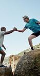 Senior friends and helping hand for hiking on rocks with fitness, adventure and support in summer. Elderly men, outdoor and climbing with lift, happy and exercise challenge by ocean in retirement