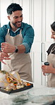 Happy couple, cooking and meal prep with turkey in kitchen for seasoning, flavor or recipe in home. Man, woman and adding ingredients with apron, spice or vegetables for thanksgiving dinner in house