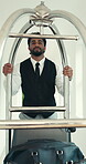 Porter, smile and luggage with man in hotel for hospitality, valet service and baggage handler. Accommodation, bellboy and booking with person and trolley in lodge for concierge and guest check in