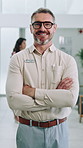 Mature man, doctor and arms crossed with face, smile and confidence with career in hospital lobby. Person, happy and medical professional in portrait with pride for healthcare services at clinic