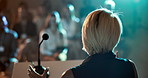 Woman, back and podium with audience in auditorium for presentation or speech in business seminar. Female person, employee or speaker with microphone or crowd for workshop or corporate trade show