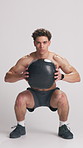 Man, squat and face in studio with medicine ball, legs and muscle development on white background. Person, weightlifting and bodybuilder with training, equipment and shirtless for workout in Colombia