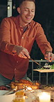 Happy man, night and turkey with serving at outdoor dinner table for thanksgiving meal or gathering. Male person, dishing and late evening with plate, chicken or candle light for feast together