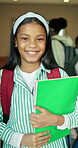 Books, face and learning with girl child in school corridor for development, future or knowledge. Education, growth and smile of happy student kid in hallway for academics, curriculum or study