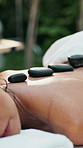 Woman, relax and hot stone massage at spa, bed and holistic treatment for back at holiday resort. Person, lava rock and service for client with rest, rehabilitation or physical therapy at lodge