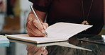 Person, hands and writing with book for checklist, agenda or daily tasks on office desk. Closeup, employee or taking notes with diary for schedule planning, reminder or record keeping in journal