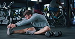 Fitness, legs and man stretching in gym for workout, training or wellness routine in morning. Health, dumbbells and male person with warm up exercise for preparing muscles on floor in sports center.