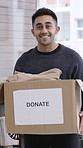 Face, man and clothes in donation box in home for non profit, portrait and community care. Cardboard, charity and person with clothing for help, humanitarian aid or package for support with smile