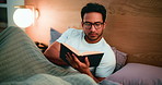 Night, man and reading book in bed with glasses for entertainment, cozy activity and literature. Late, person and comfortable with eyewear in apartment for fiction story, novel and relaxing hobby.