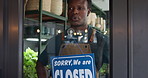 Happy, closed sign and black man by door in store for sustainability, plants or greenery at small business. Board, customer service and African botanist with announcement at at eco friendly nursery.
