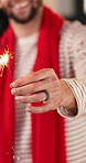 Christmas, hand and sparkler with man in home living room for celebration or festive tradition. Fingers, fireworks and winter season with happy person closeup in apartment for December holidays