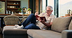 Reading, books and senior man on sofa to enjoy literature, story and literacy in home. Retirement, living room and elderly person relax with novel for me time, hobby or fiction for knowledge in house