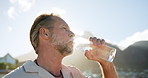 Outdoor, mature or man drinking water with bottle, mineral liquid or hydration for electrolytes balance. Thirst, low angle or healthy person with refreshing beverage for nutrients, wellness or nature
